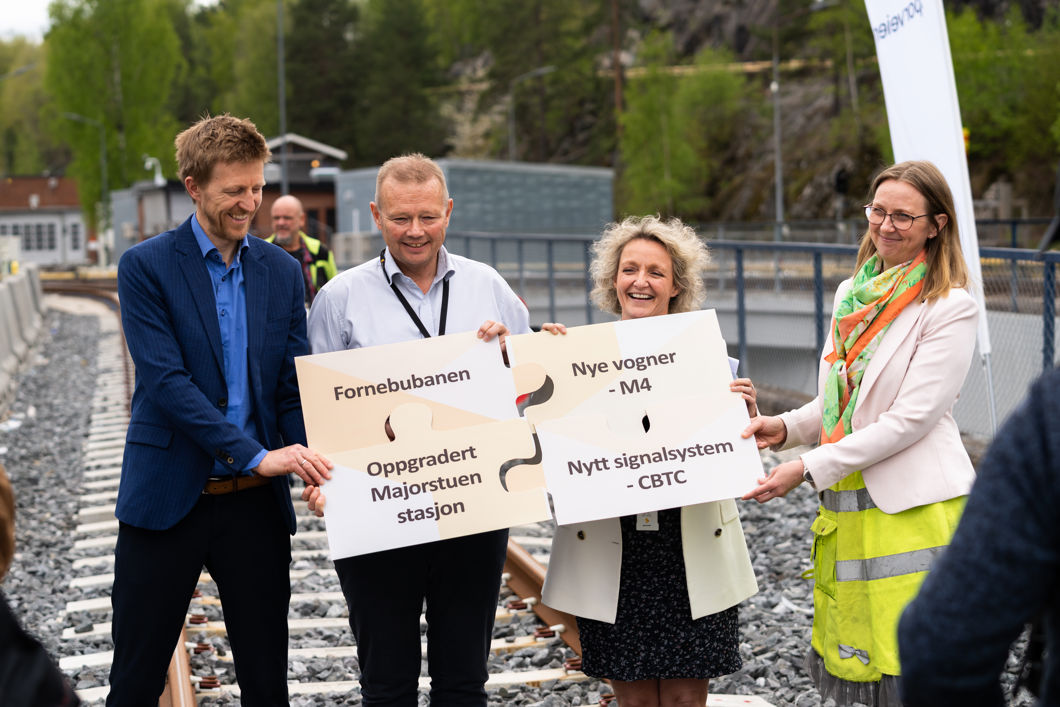 Bildet viser fire mennesker som holder frem et puslespill i papp, der hver brikke har navnet til en av de fire prosjektene som utgjør T-baneløftet.
